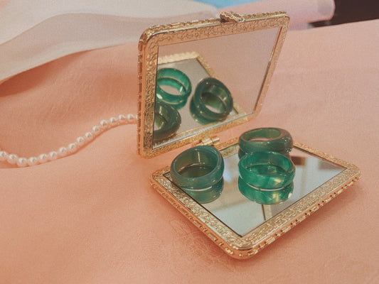 Three jade rings from Leehwa Wedding & House of Leehwa mounted on a hand mirror with a string of pearls and peach colored hanbok skirt in the background